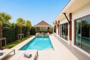 A modern outdoor swimming pool with lounge chairs, a covered seating area, and a view of a poolside building. - Secluded New Villa with Private Pool 2 Bedrooms (Tambon Rawai)
