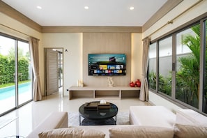 A modern living room with a flat-screen TV mounted on the wall, a glass coffee table, and a sofa.