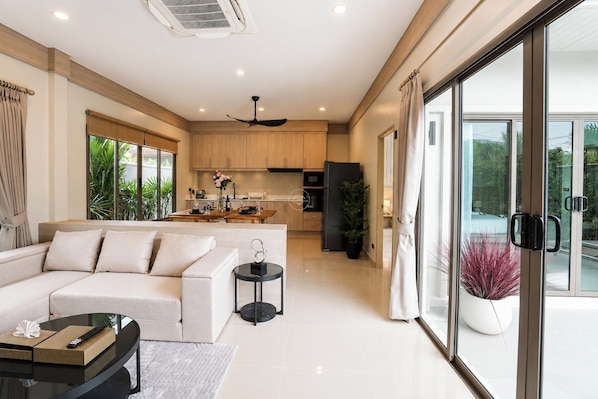 A modern living room with a sofa, a glass coffee table, and a dining area with a table and chairs. - Secluded New Villa with Private Pool 2 Bedrooms (Tambon Rawai)
