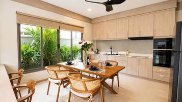 A modern kitchen with wooden cabinets, a dining table with chairs, and a ceiling fan.
