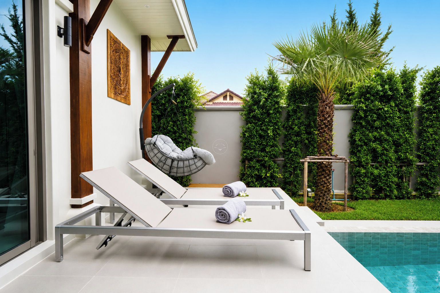 A modern outdoor pool area with two lounge chairs, a hanging chair, and a neatly arranged towel.