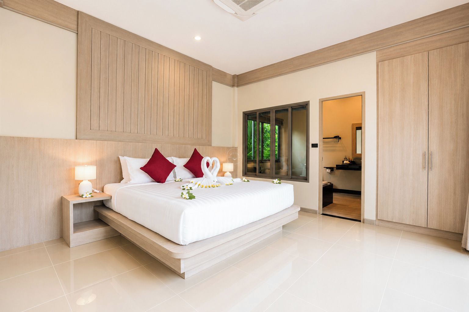 A modern hotel bedroom with a large bed, wooden headboard, bedside lamps, and a view of the bathroom.
