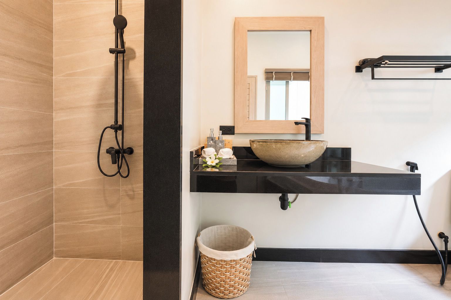 A modern bathroom with a black countertop, a large mirror, a vessel sink, and a shower with a black hose.