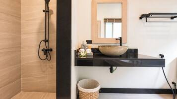 A modern bathroom with a black countertop, a large mirror, a vessel sink, and a shower with a black hose.