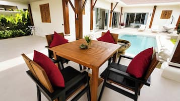 A wooden table with chairs, a pool, and a view of the house.