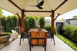 A covered patio with a table and chairs, surrounded by greenery and a decorative bird statue. - Secluded New Villa with Private Pool 2 Bedrooms (Tambon Rawai)