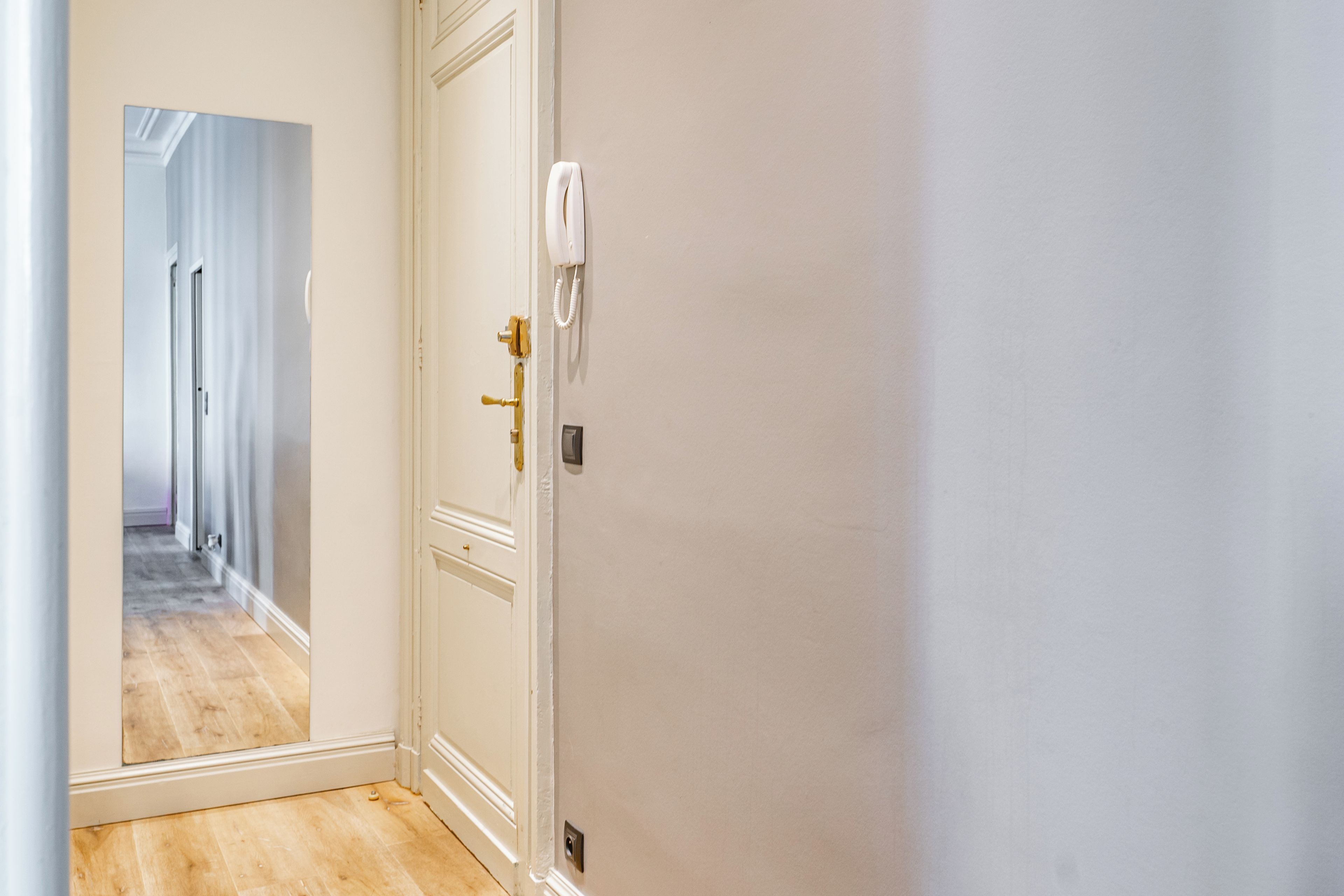 A hallway with a white door, a wall-mounted phone, and a wooden floor.