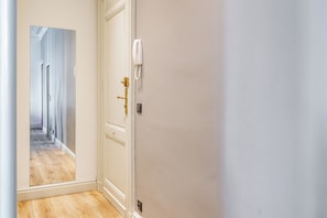 Un couloir avec une porte blanche, un téléphone fixé au mur et un plancher en bois.
