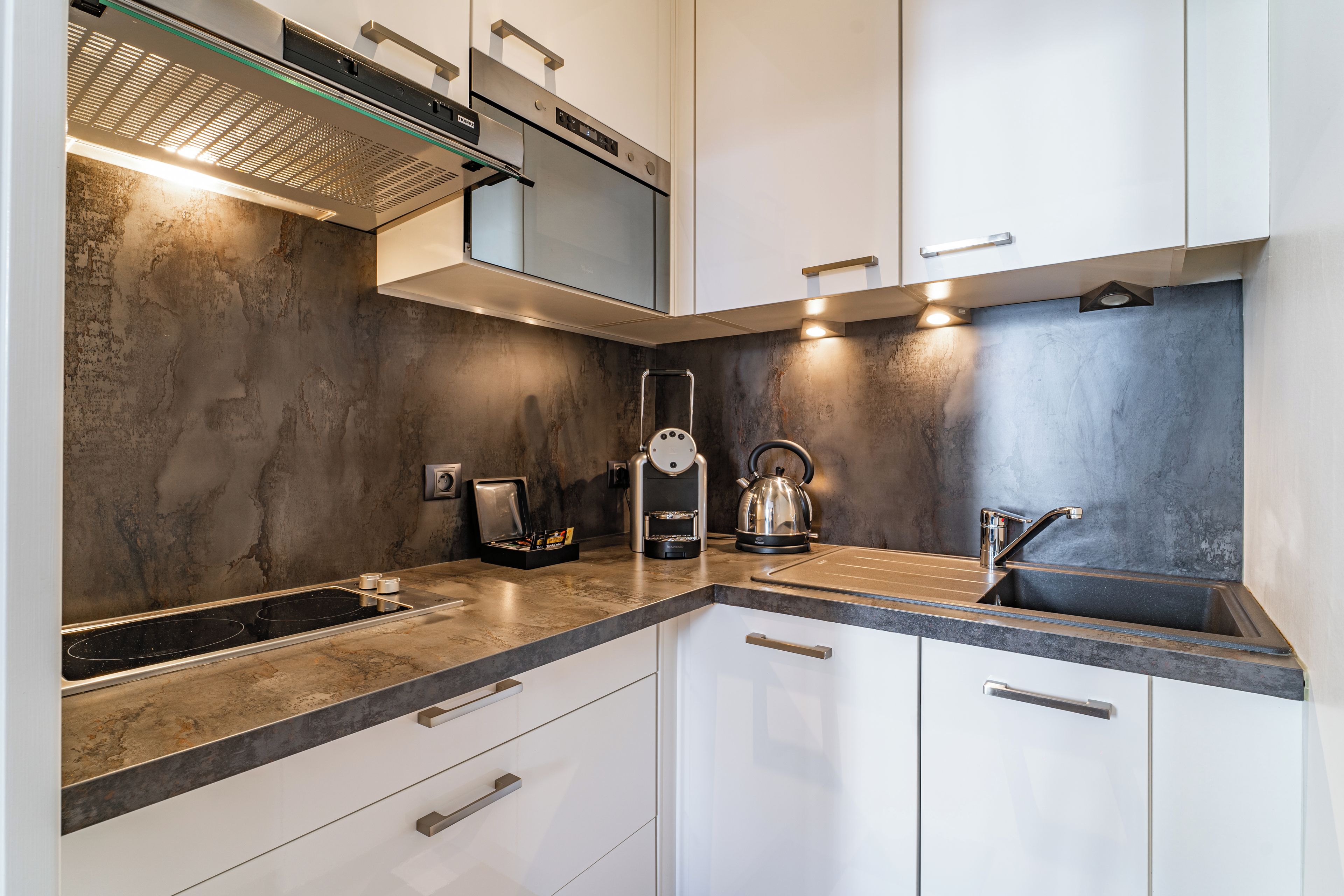 A modern kitchen with a built-in stove, a kettle, and a coffee machine.