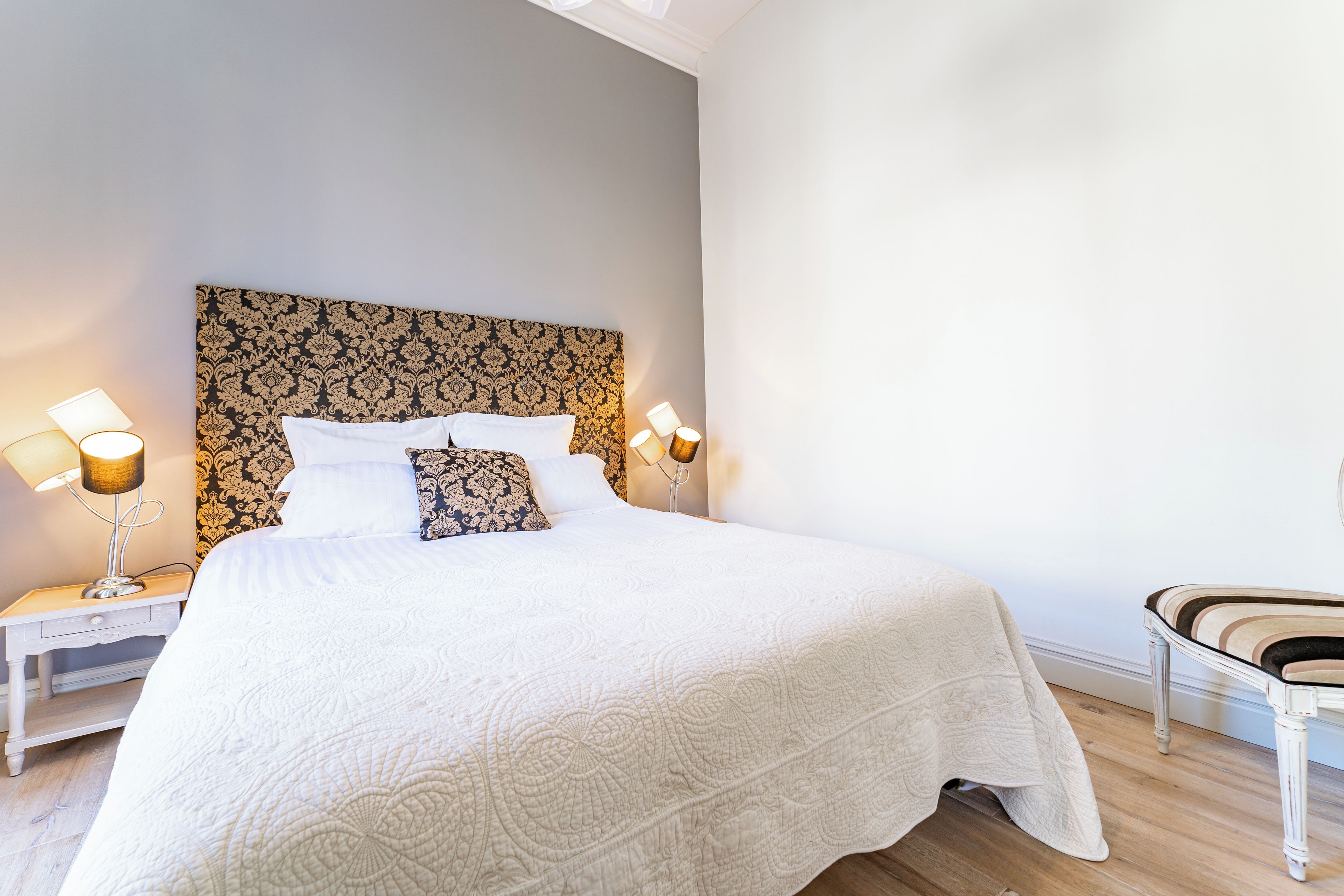 Un letto rifatto con una testiera decorata, due lampade ai lati del letto e una sedia con un cuscino.
