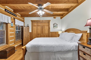 Een slaapkamer met houten vloer, een bed, een plafondventilator, een kledingkast en een raam met zonwering.