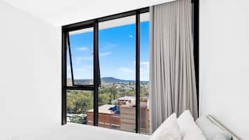 A bedroom with a large window, a bed, and a view of a cityscape.