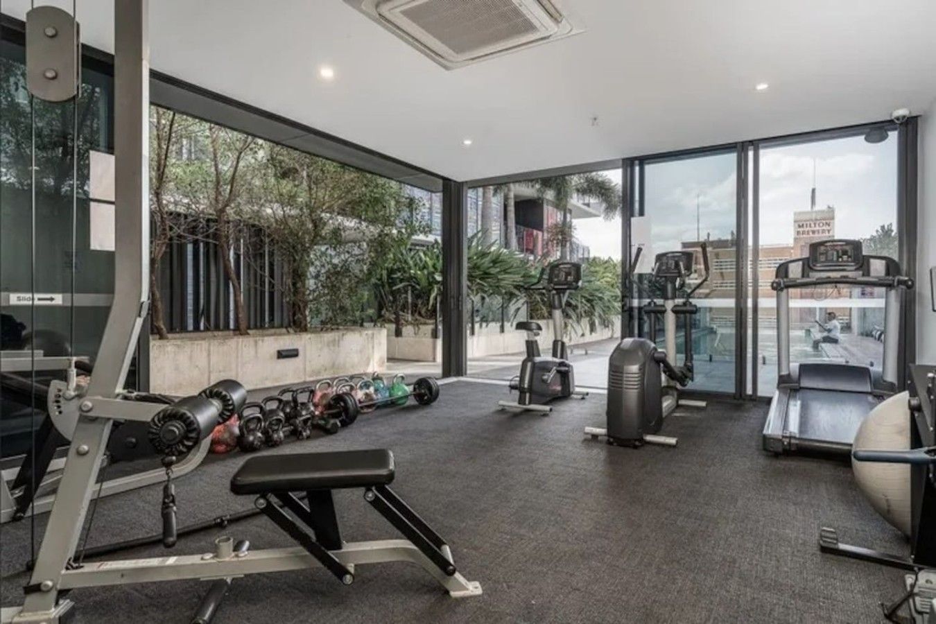 Ein Fitnessstudio mit verschiedenen Trainingsgeräten, großen Fenstern und Blick nach draußen.