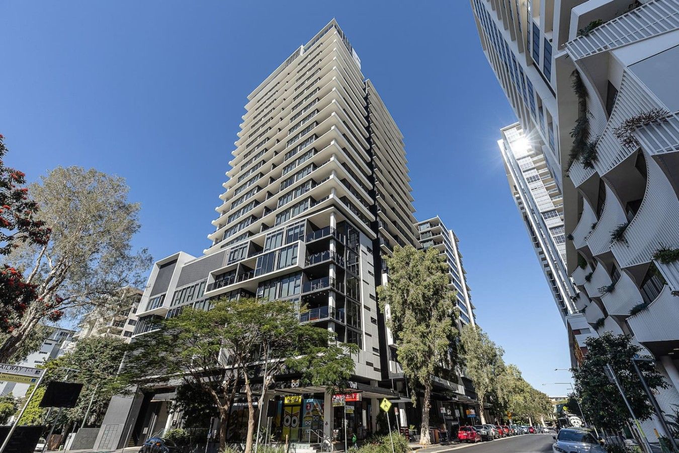 Un immeuble moderne de grande hauteur, doté de nombreux balcons et entouré d’arbres et d’autres bâtiments.