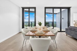 En spiseplads med et bord dækket til seks personer, store skydedøre af glas og en grå sofa.