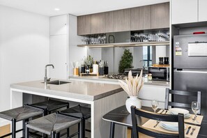A modern kitchen with a central island, bar stools, a dining table set for two, and a built-in oven. - Luxe 1BR | Queen’s Wharf | Casino & Pool (Brisbane City)