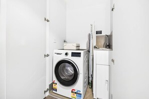 A compact, white laundry room with a front-loading washing machine, a dryer, and a small cabinet. - Luxe 1BR | Queen’s Wharf | Casino & Pool (Brisbane City)