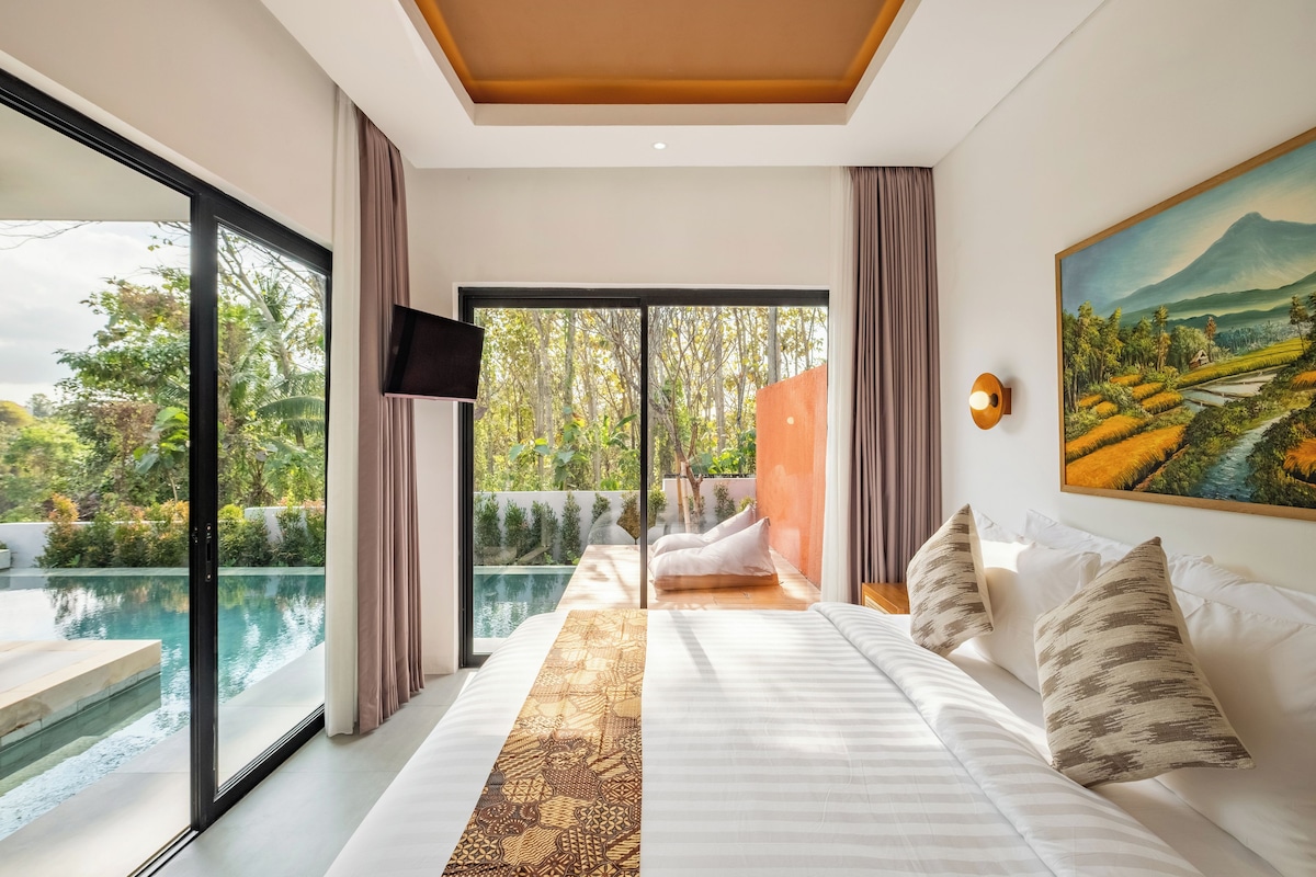 Un dormitorio con una cama grande, un cuadro, un televisor y vistas a una piscina y jardín.