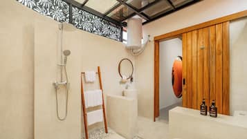 A modern bathroom with a shower, a bathtub, a wooden door, and a vanity with toiletries.