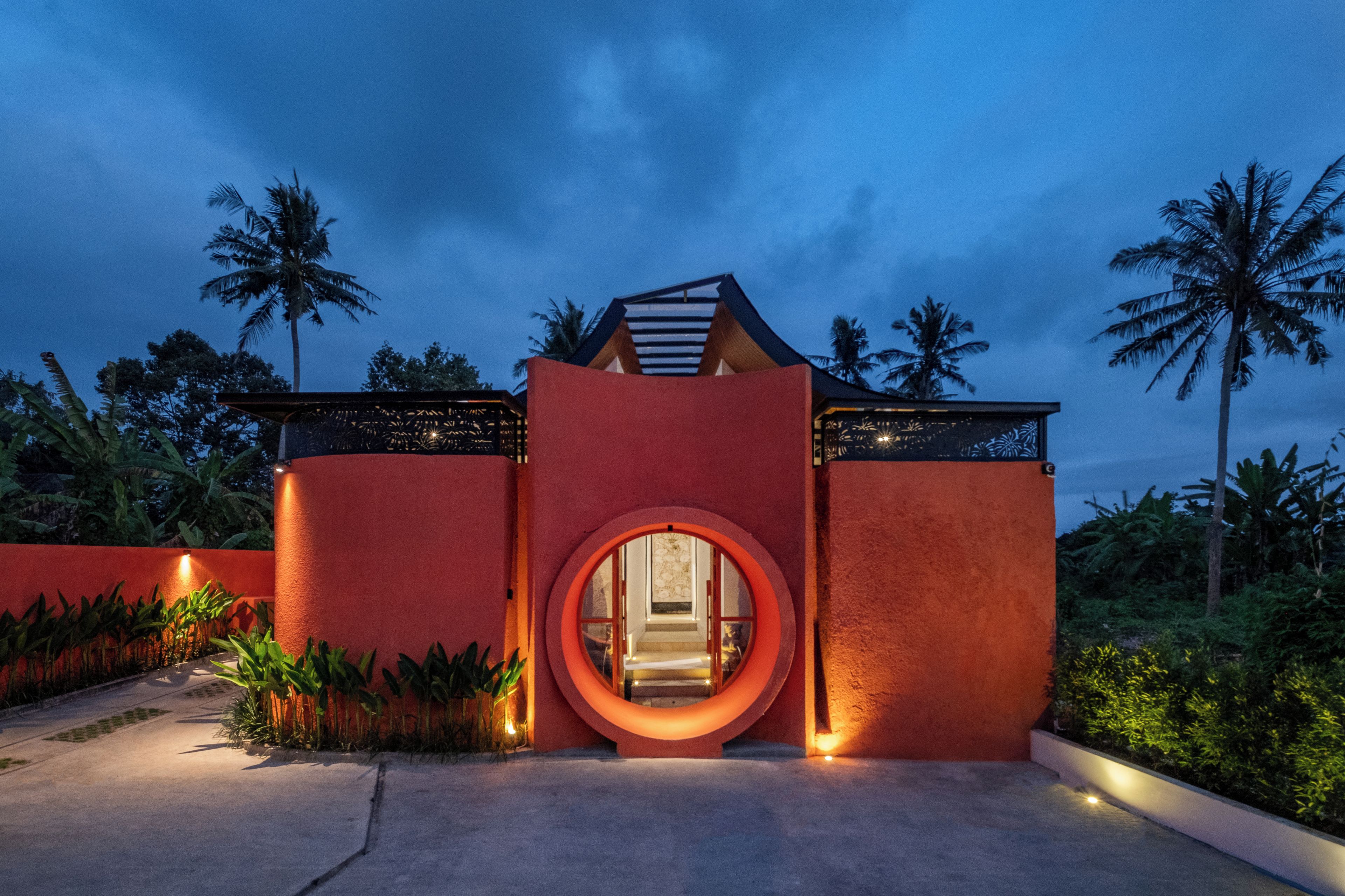 A modern building with a circular entrance, surrounded by palm trees and greenery.