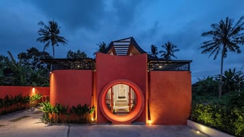 A modern building with a circular entrance, surrounded by palm trees and greenery.