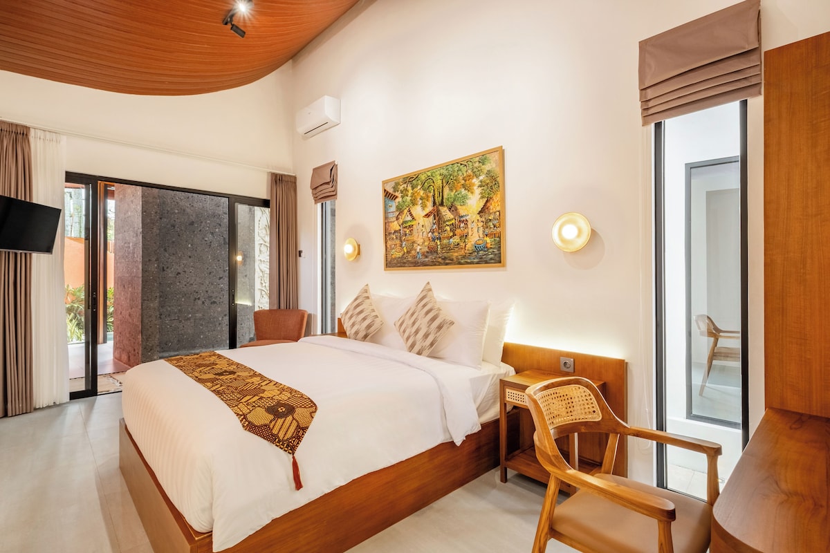 Una habitación de hotel con una cama grande, un cuadro en la pared, un televisor de pantalla plana y una ventana con cortinas.