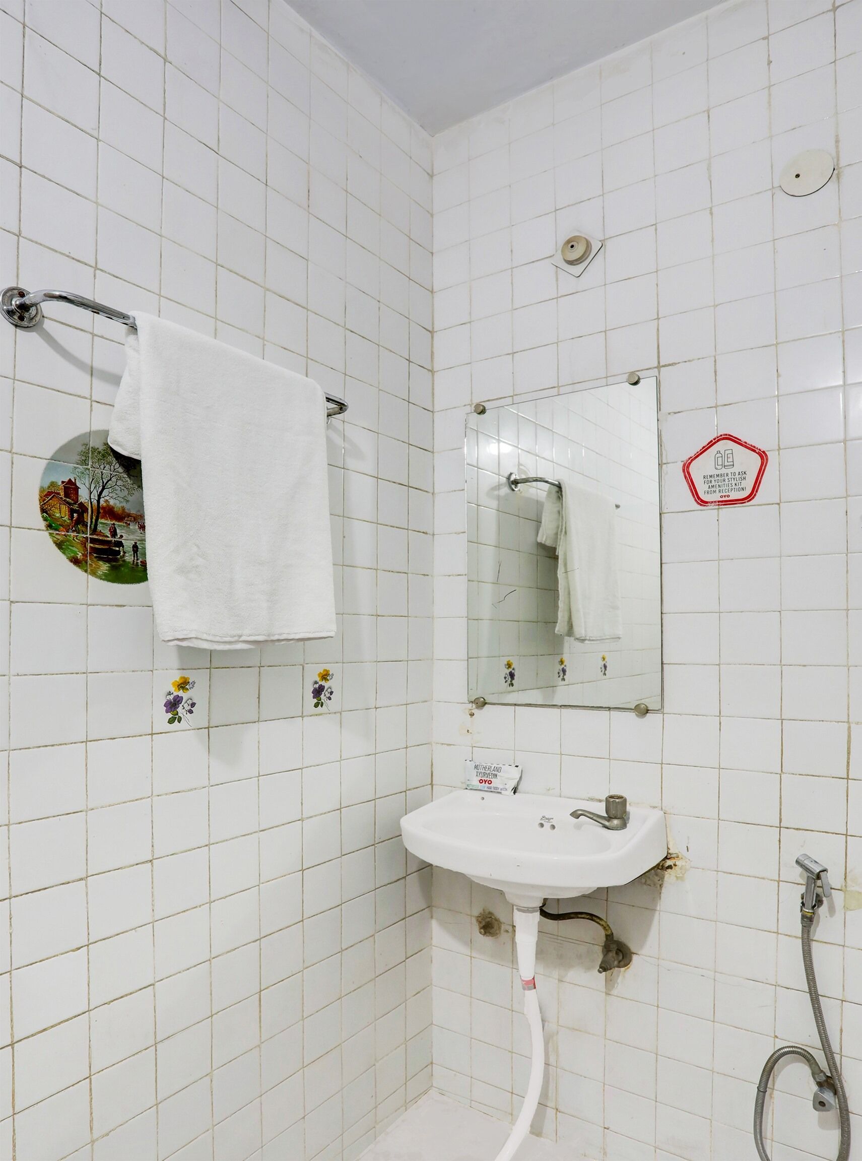 Une salle de bain avec des murs carrelés de carreaux blancs, un lavabo blanc, un miroir et un porte-serviettes.
