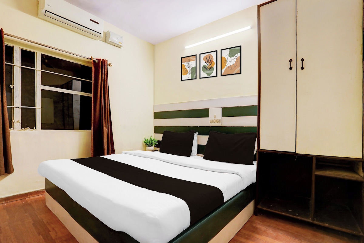 A hotel room with a bed, a wardrobe, a window with curtains, and wall-mounted artwork.