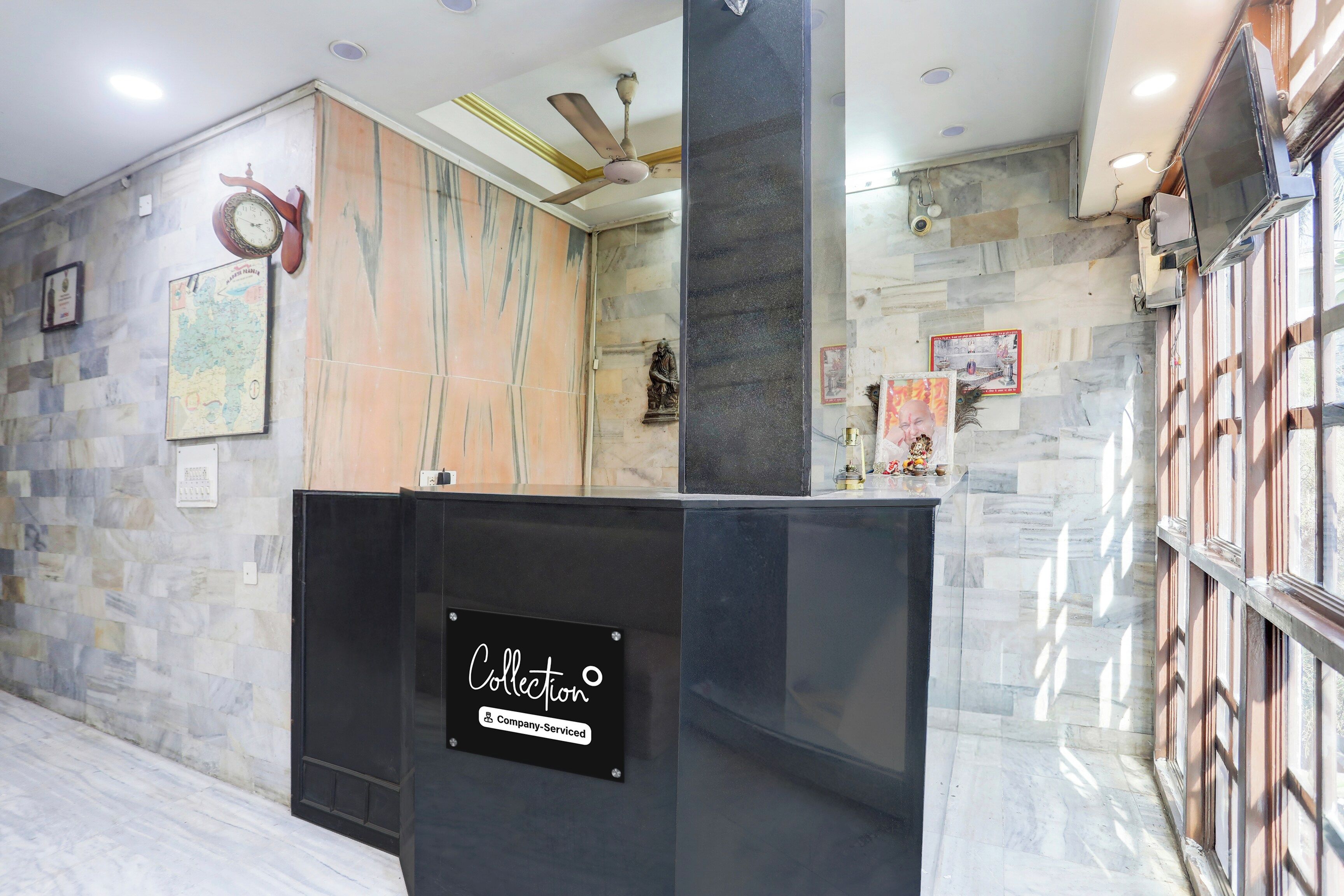 Un área de recepción con pared de mármol, un reloj y un cartel que dice 'Collection Company-Serviced'.