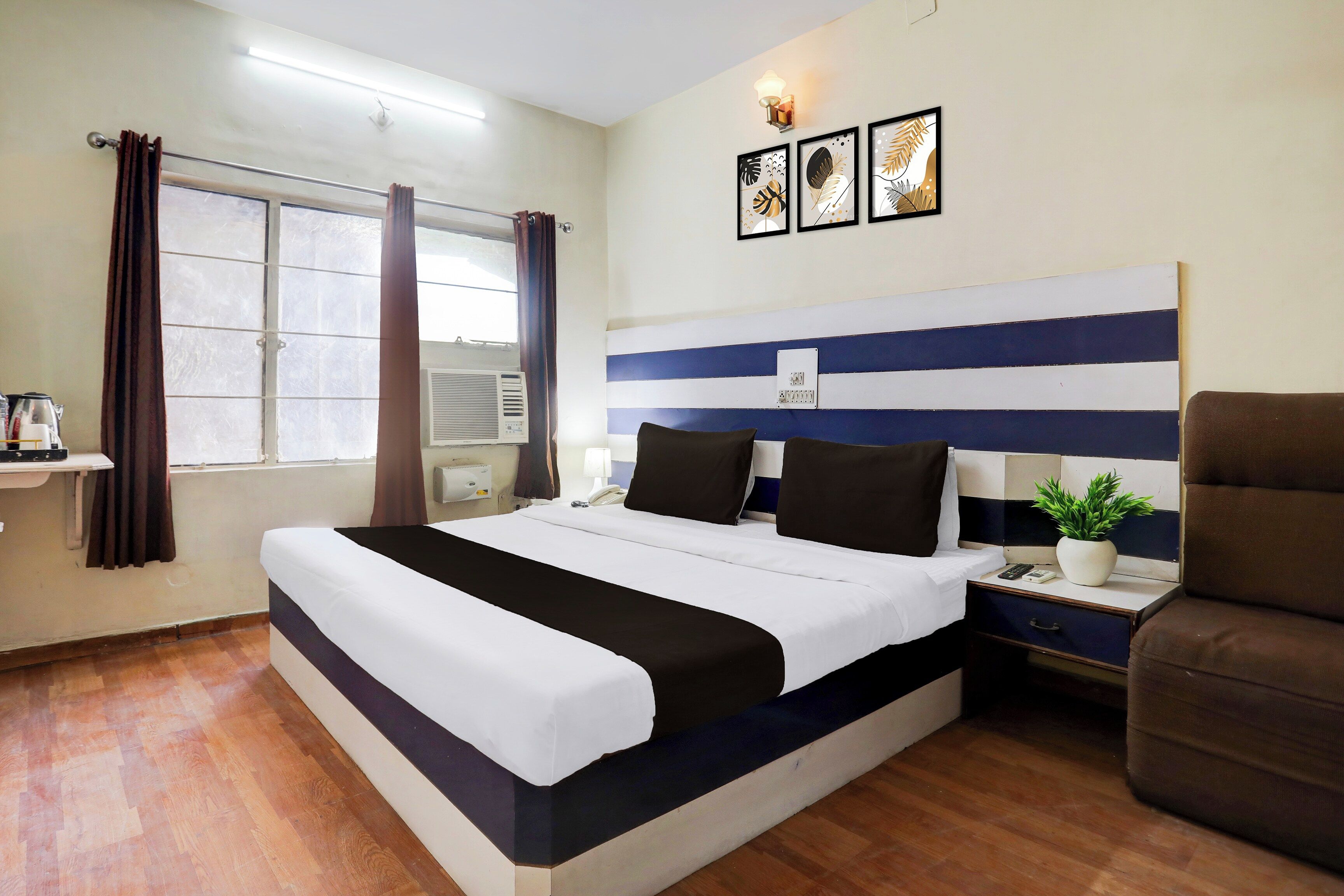 A hotel room with a large bed, a bedside table with a lamp, a potted plant, and a chair.