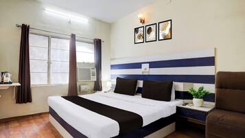 A hotel room with a large bed, a bedside table with a lamp, a potted plant, and a chair.