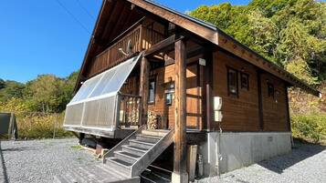 A wooden cabin with a covered porch, a staircase leading to the entrance, and a gravel driveway.