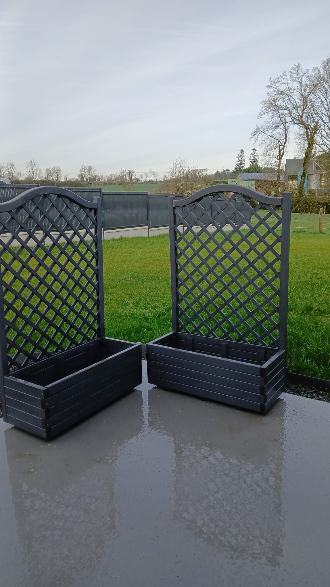 Een metalen hekwerk met een rasterwerkpatroon, dat uitkomt op een gazon met een waterpartij op de achtergrond.