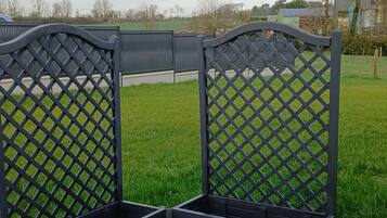Een metalen hekwerk met een rasterwerkpatroon, dat uitkomt op een gazon met een waterpartij op de achtergrond.