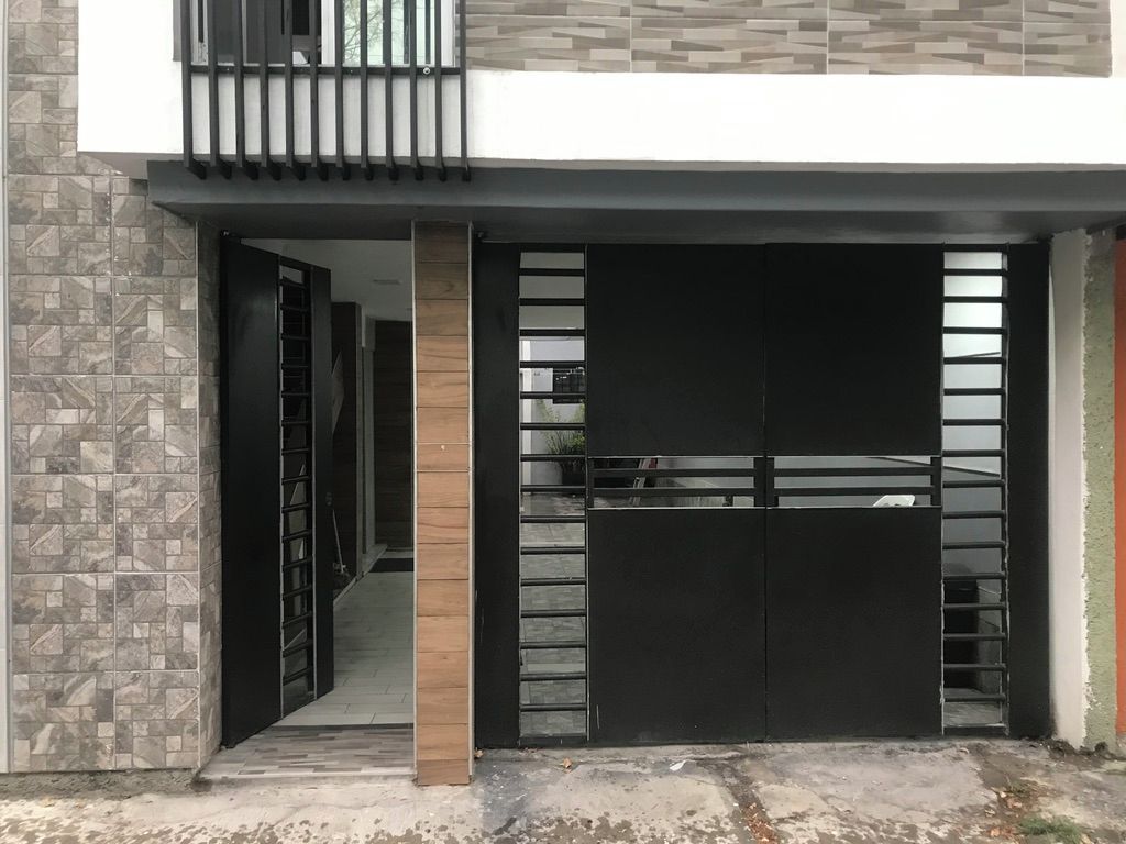 Une entrée moderne, avec un portail noir, une colonne en bois et un mur recouvert de carreaux.