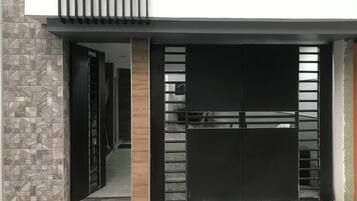 Une entrée moderne, avec un portail noir, une colonne en bois et un mur recouvert de carreaux.