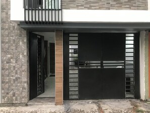 Une entrée moderne, avec un portail noir, une colonne en bois et un mur recouvert de carreaux.