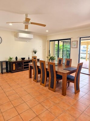A dining area with a wooden table and chairs, a ceiling fan, and a view through a glass door.