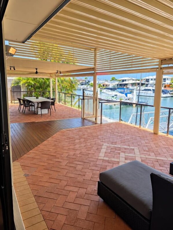 A covered outdoor area with a table and chairs, a sofa, and a view of a marina with boats.