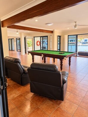Amplia habitación con mesa de billar, dos sofás de cuero y un amplio ventanal con vistas al exterior.