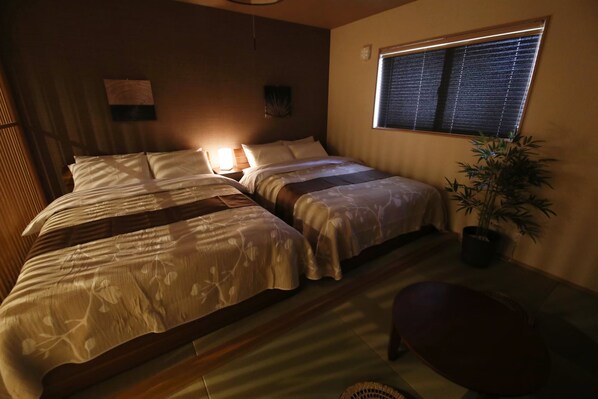 A room with two beds, a bedside table, a potted plant, and a window with blinds. - Kamon Inn Uji 2 UKx (Uji)