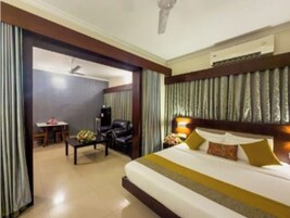 A hotel room with a large bed, a desk, a chair, and a dining table.