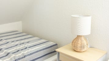 A bedroom with a bed, a bedside table with a lamp, and a wall-mounted shelf.