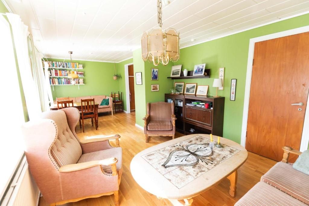Een gezellige woonkamer met een bank, fauteuil en een salontafel. Er staat een boekenplank vol boeken en er is een deur aan de rechterkant.