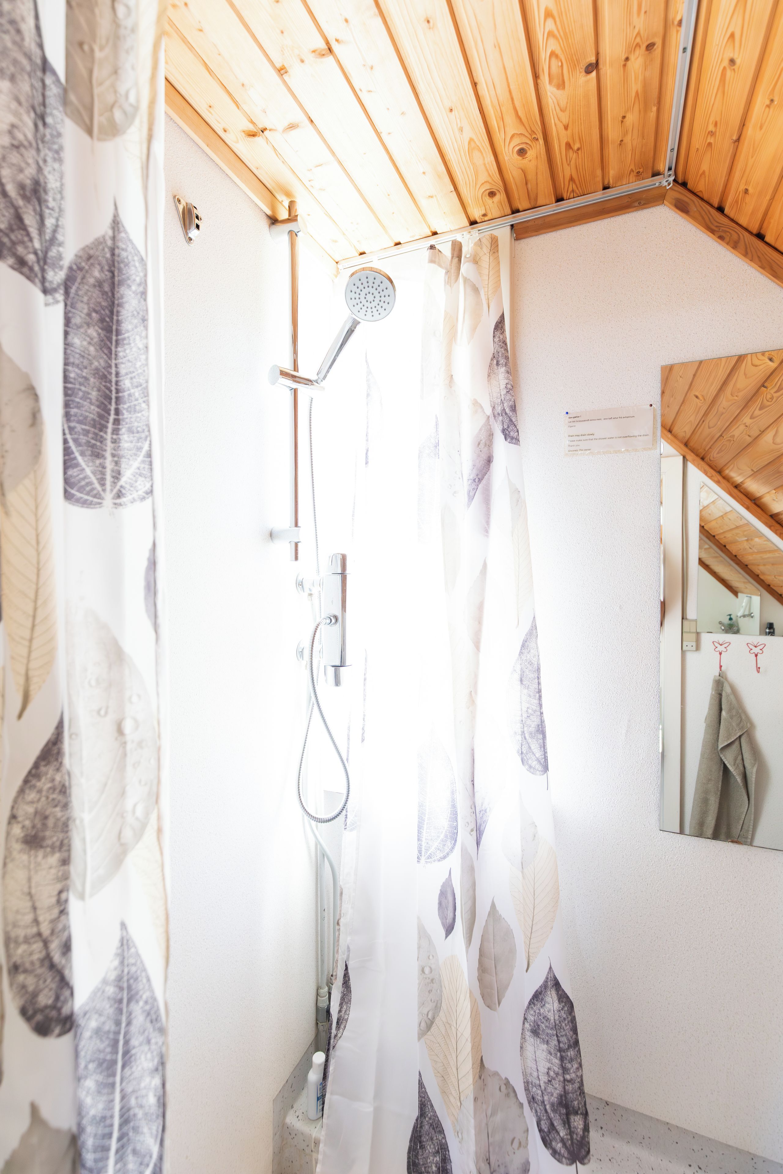 A shower area with a wooden ceiling, a showerhead, and a curtain with a leaf pattern.