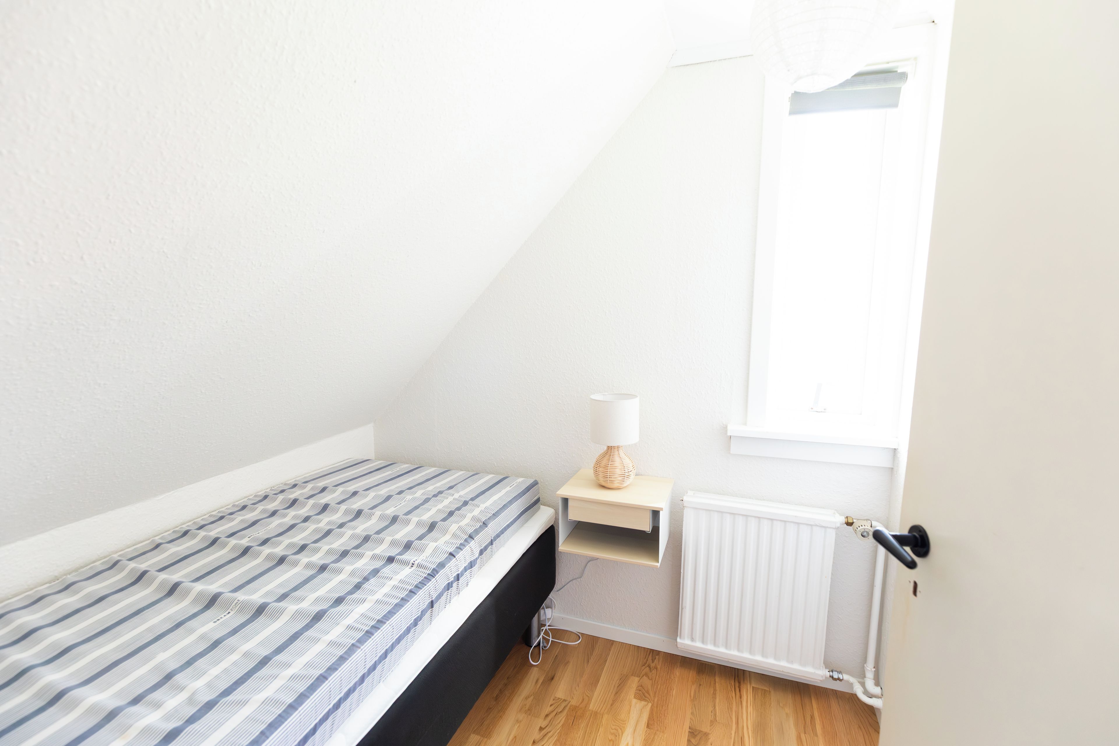 A small, single-bed room with a sloped ceiling, a radiator, and a window.