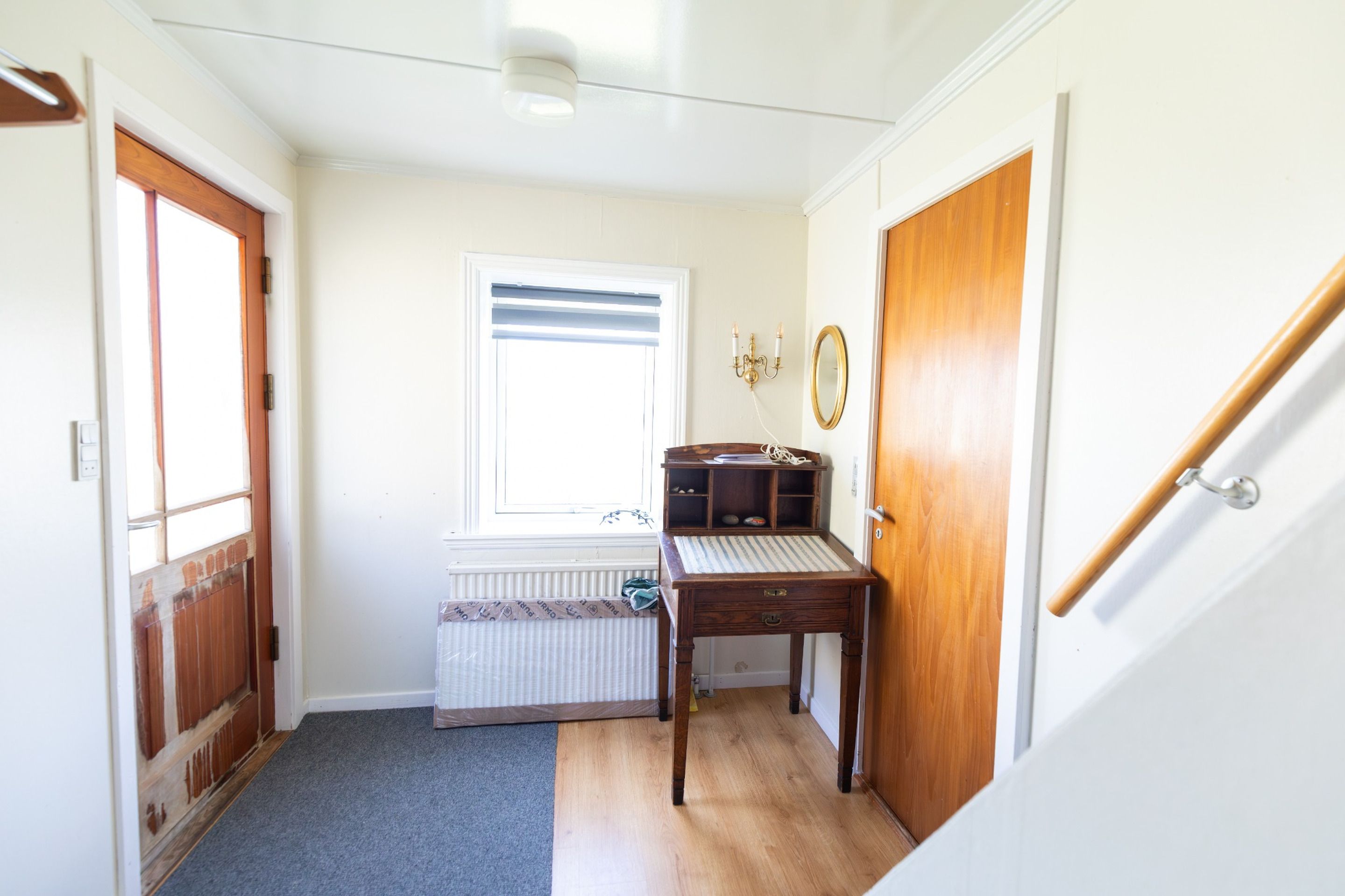 A hallway with a radiator, a wooden desk, a mirror, and a door.