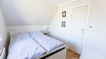 A small, single-bed room with a sloped ceiling, a bedside table with a lamp, and two framed pictures on the wall.