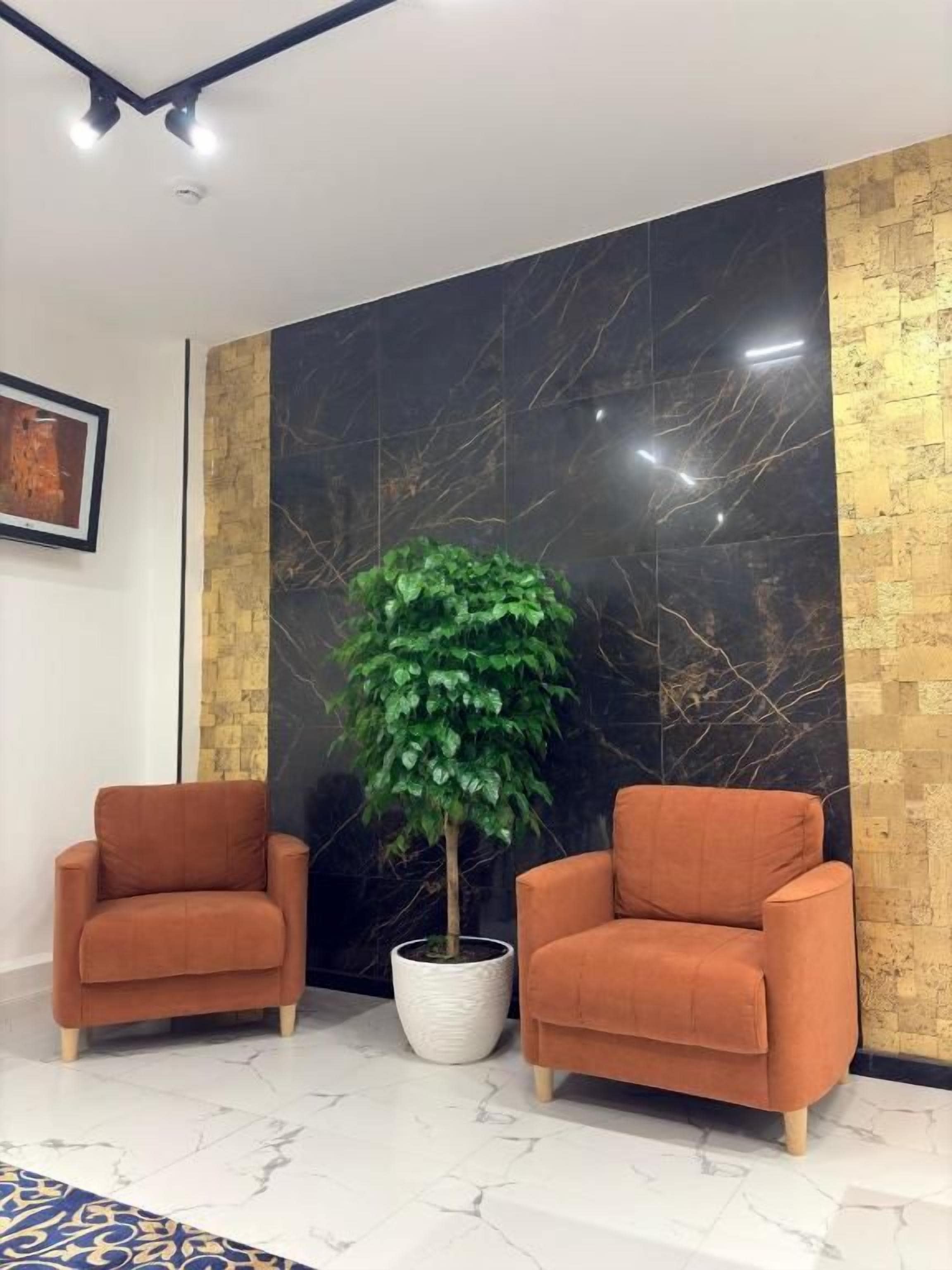 A room with two orange armchairs, a potted plant, a marble wall, and a framed picture on the wall.