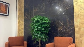 A room with two orange armchairs, a potted plant, a marble wall, and a framed picture on the wall.